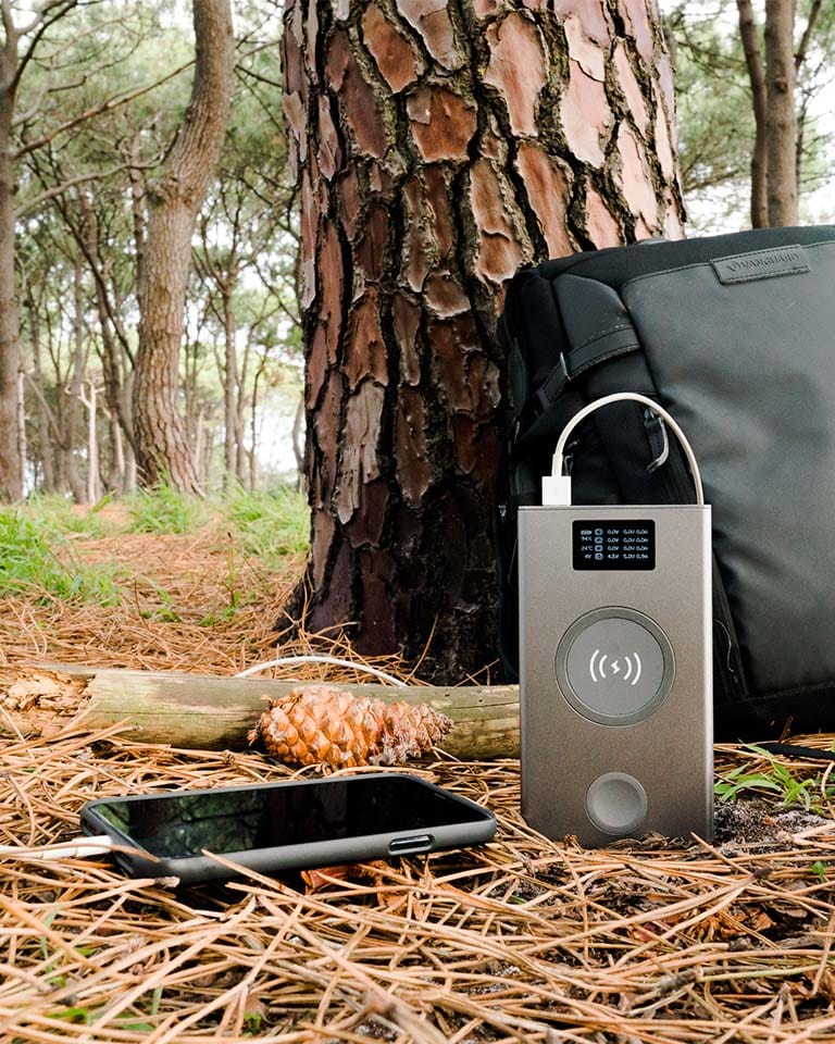 Image of Graphene Powerbank, Flash Pro Plus charging iPhone in the forest, with 25000mAh large battery capacity, OLED display, USB-C 100W fast charging. An iPhone 14 is being charged on the MagSafe compatible wireless charging up to 15W. An Apple Watch is being charged on the separate Apple Watch charging pad supporting up to 5W. Perfect for Apple users on the go. 