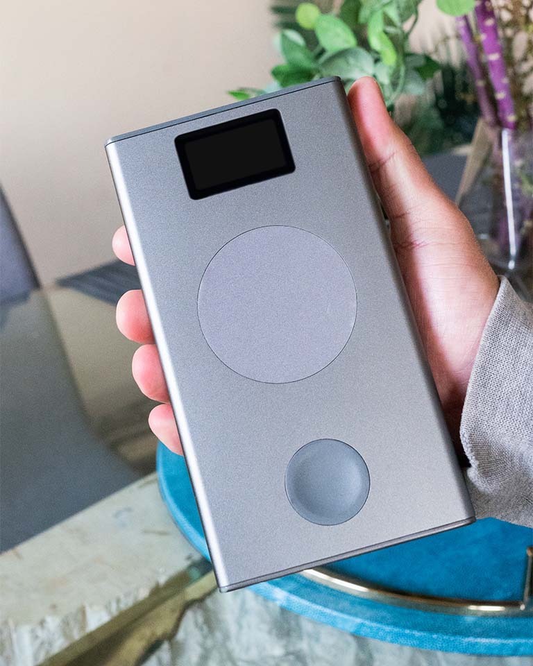 Image of handing holding Graphene Powerbank, Flash Pro Plus, with 25000mAh large battery capacity, OLED display, USB-C 100W fast charging. An iPhone 14 is being charged on the MagSafe compatible wireless charging up to 15W. An Apple Watch is being charged on the separate Apple Watch charging pad supporting up to 5W. Perfect for Apple users on the go. 