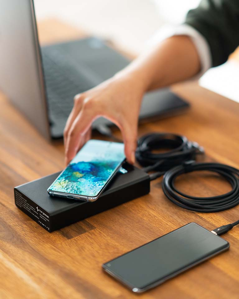 Image of person placing samsung phone on wireless charger of Graphene Powerbank, Flash Pro. 25000mAh large battery capacity, OLED display, USB-C 100W fast charging, wireless charger up to 15W, and Perfect for Android mobile and laptop users 